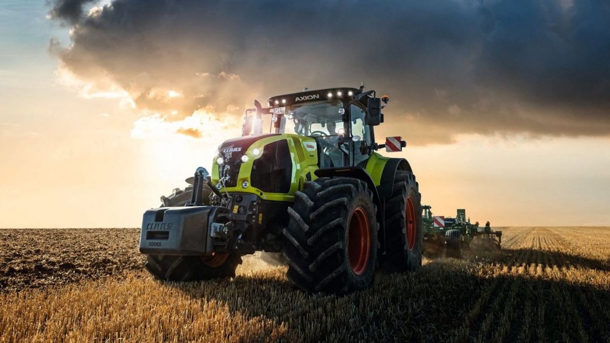 Traktor mit Anhänger der Firma Claas fährt auf einer Straße in einem landwirtschaftlichen Gebiet