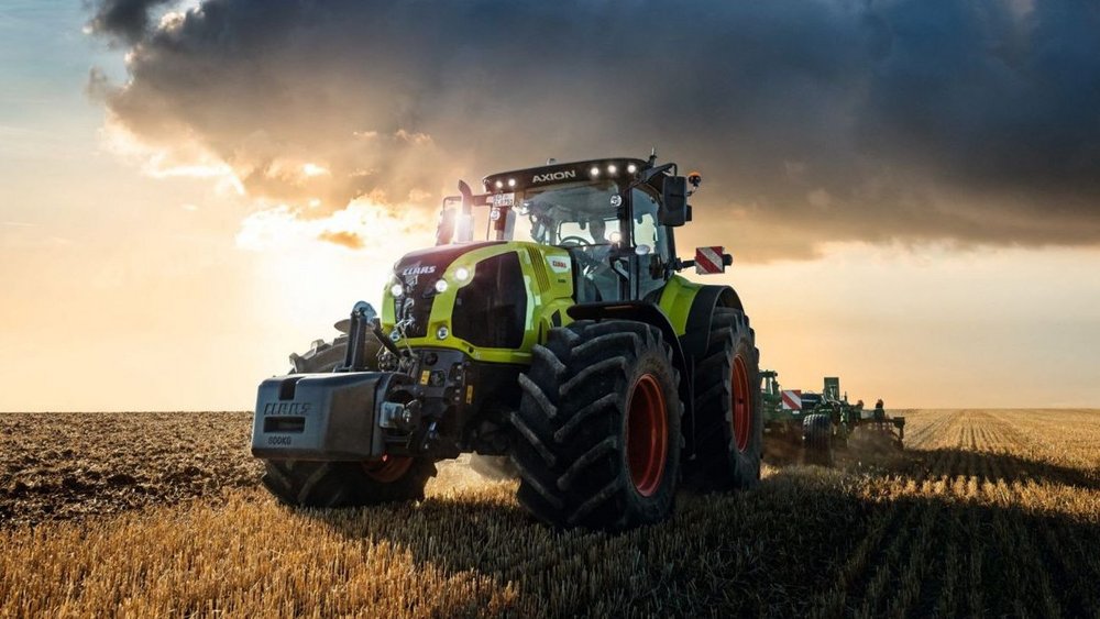 Traktor mit Anhänger der Firma Claas fährt auf einer Straße in einem landwirtschaftlichen Gebiet