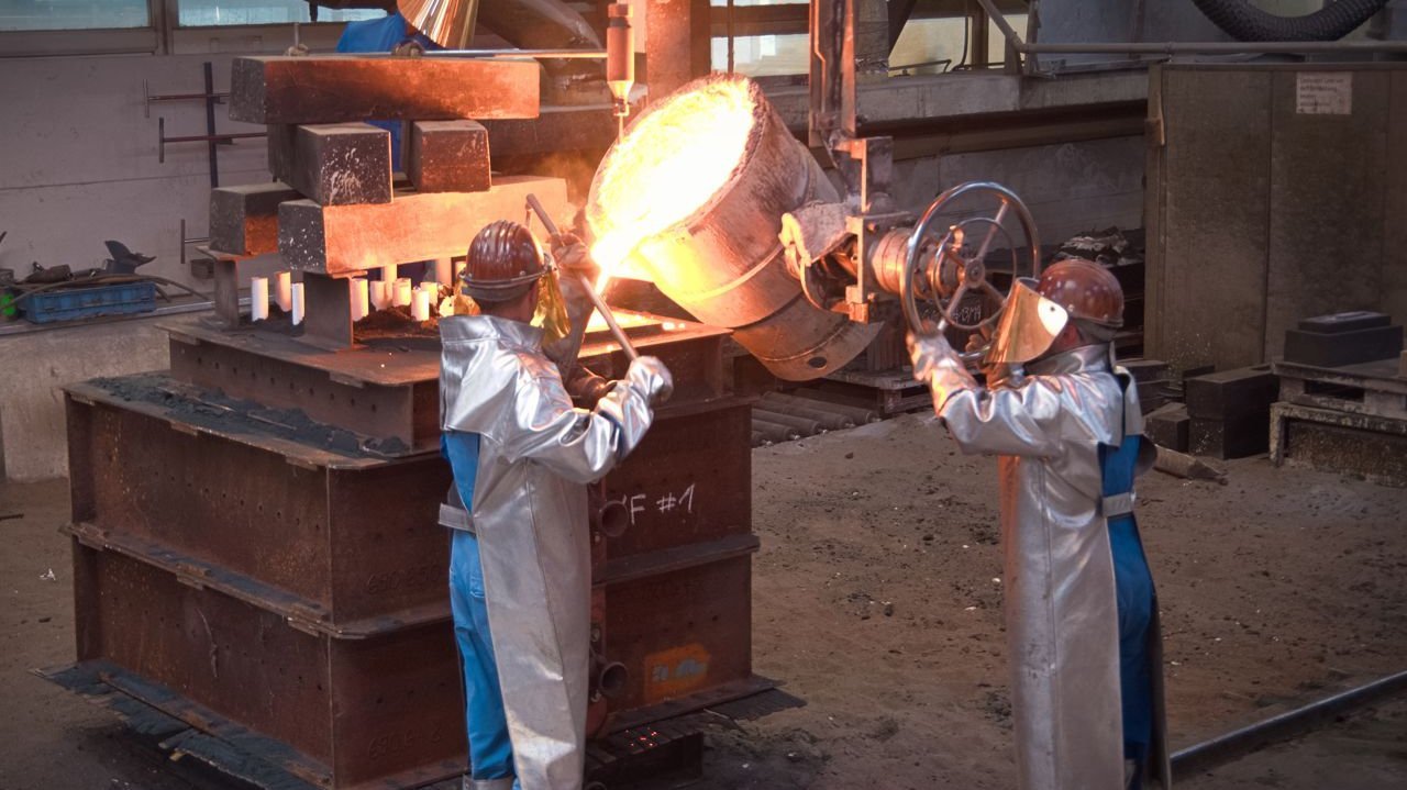 Foundry worker casting steel on particularly large sand mold 